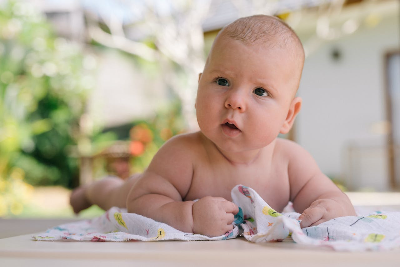 Charming baby on a blanket enjoying tummy time in a sunny outdoor setting, capturing innocence and curiosity.